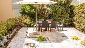 An outdoor patio with a table and chairs, surrounded by a garden with various plants and a gravel path. - Apartments "Labinac" Pula- Apartment I (Pula)