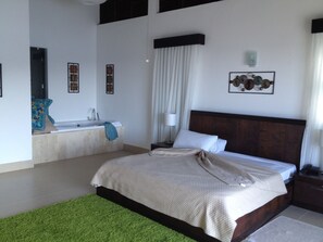 A bedroom with a large bed, a bathroom with a bathtub, and a green rug.