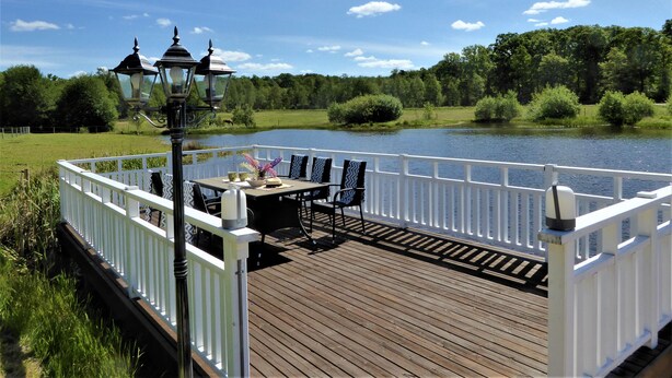 Een houten terras met een witte balustrade, een tafel met stoelen en een lamp.