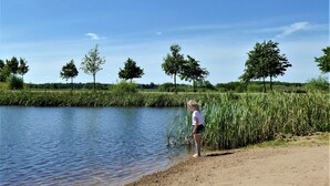 Een zandstrand met kalm water, bomen en een heldere lucht.