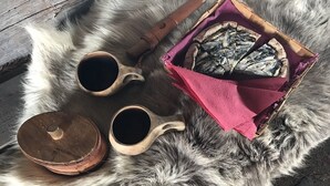 A wooden table with two wooden cups and a basket of dried fish on a fur surface. - Lentiira Holiday Village (Kuhmo)