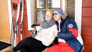 Two people sitting on a bench outside a building with skis leaning against the wall. - Lentiira Holiday Village (Kuhmo)