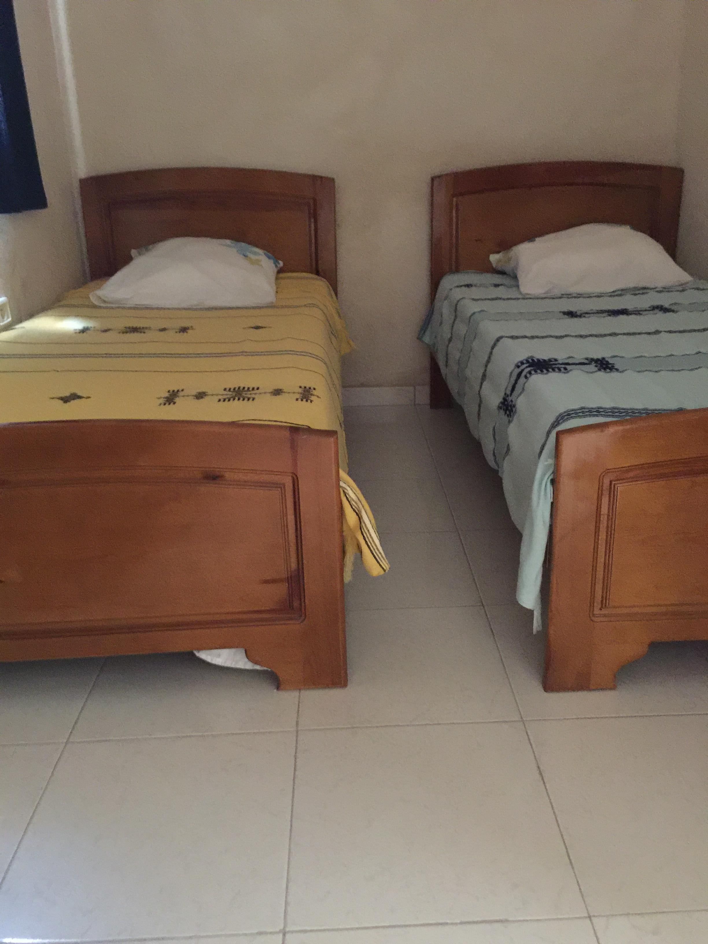 Dos camas de madera con cabeceros, suelo de baldosas y una pared lisa.