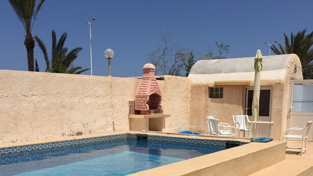 A swimming pool with steps leading up to it, surrounded by a beige wall and palm trees. - Independent Villa With Private Pool, Covered Parking (Mezraia)