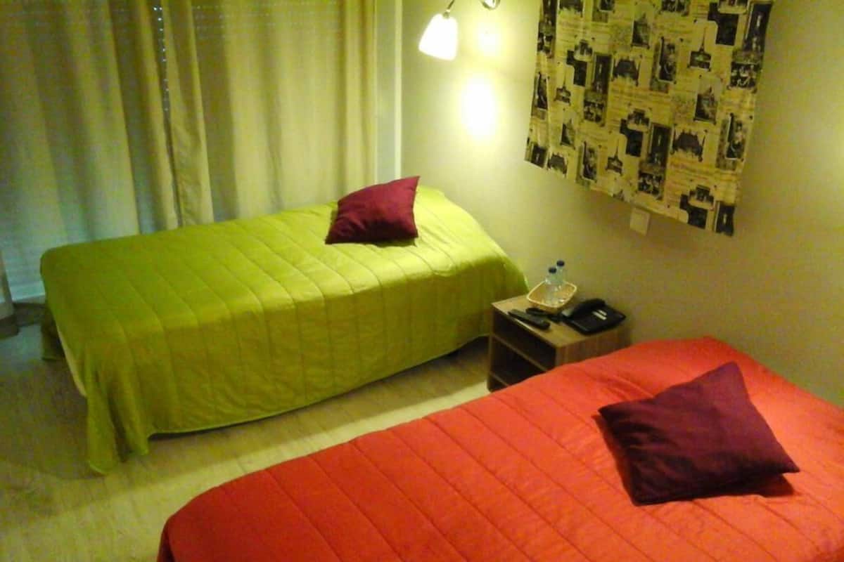 Two single beds with different colored bedding, a nightstand with a lamp, and a wall with a patterned curtain.