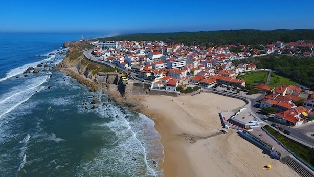 An aerial view of a coastal town with a beach, houses, and a lighthouse. - Hostel Paris (Marinha Grande)