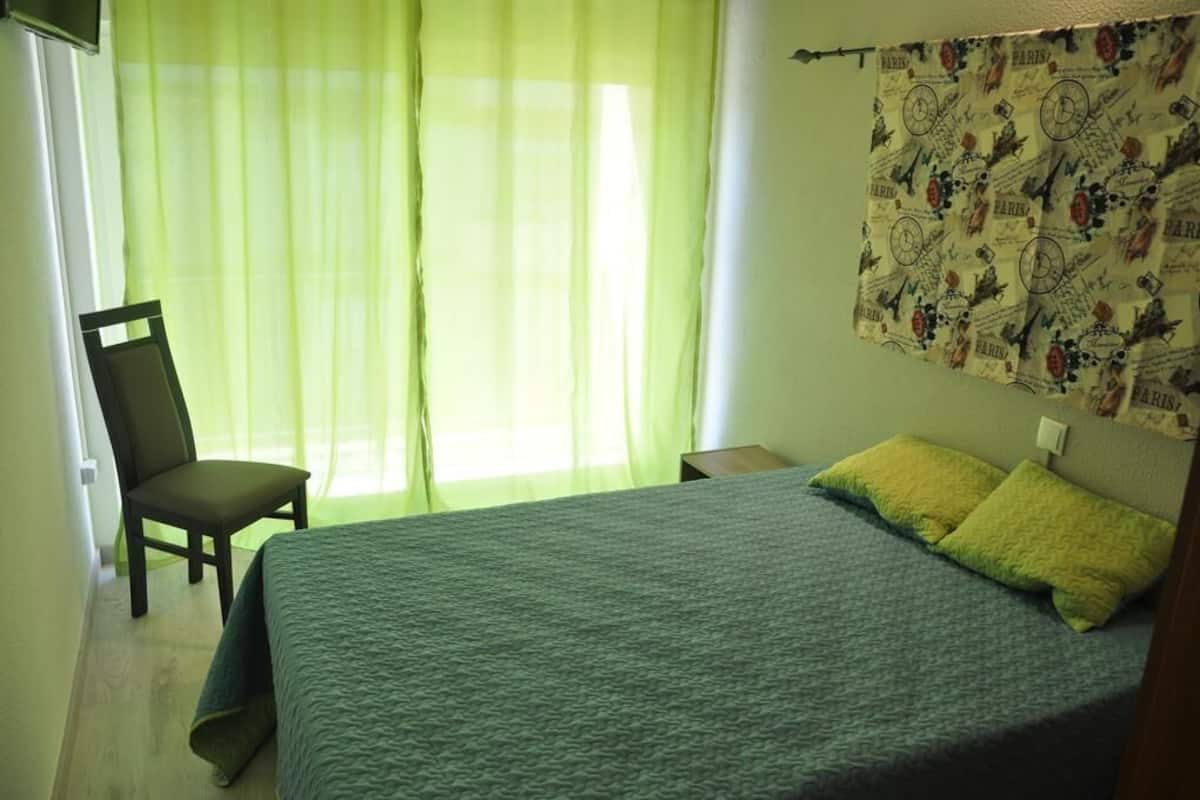 A bedroom with a bed, a chair, and a window with sheer curtains.