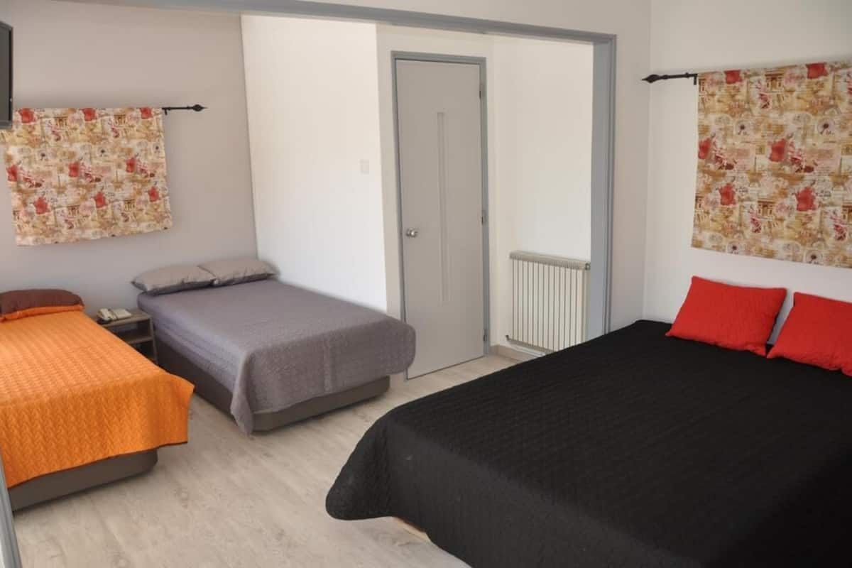 A room with two beds, one with an orange bedspread and another with a black bedspread, a grey wall, a door, and a radiator.