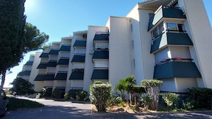 Un edificio de varios pisos con un diseño arquitectónico moderno, que cuenta con balcones y un área de estacionamiento al frente.