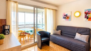 Una sala de estar moderna con sofá, cafetera, mesa de comedor con sillas y vistas al mar a través de grandes ventanales.
