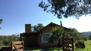 A small, single-story house with a wooden gate, a palm tree, and a clear blue sky. - Rent Villa General Belgrano, Calamuchita (Los Reartes)