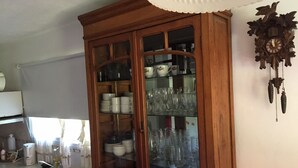 A kitchen with a wooden cabinet containing dishes and glassware, a sink, and a wall-mounted clock. - Rent Villa General Belgrano, Calamuchita (Los Reartes)