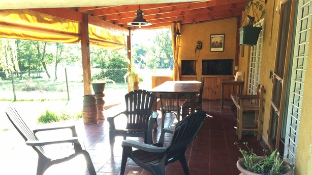 A covered patio area with a table and chairs, a large potted plant, and a television mounted on the wall. - Rent Villa General Belgrano, Calamuchita (Los Reartes)