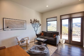 A living room with a sofa, coffee table, and a chair. There is a large window with a view of the desert.