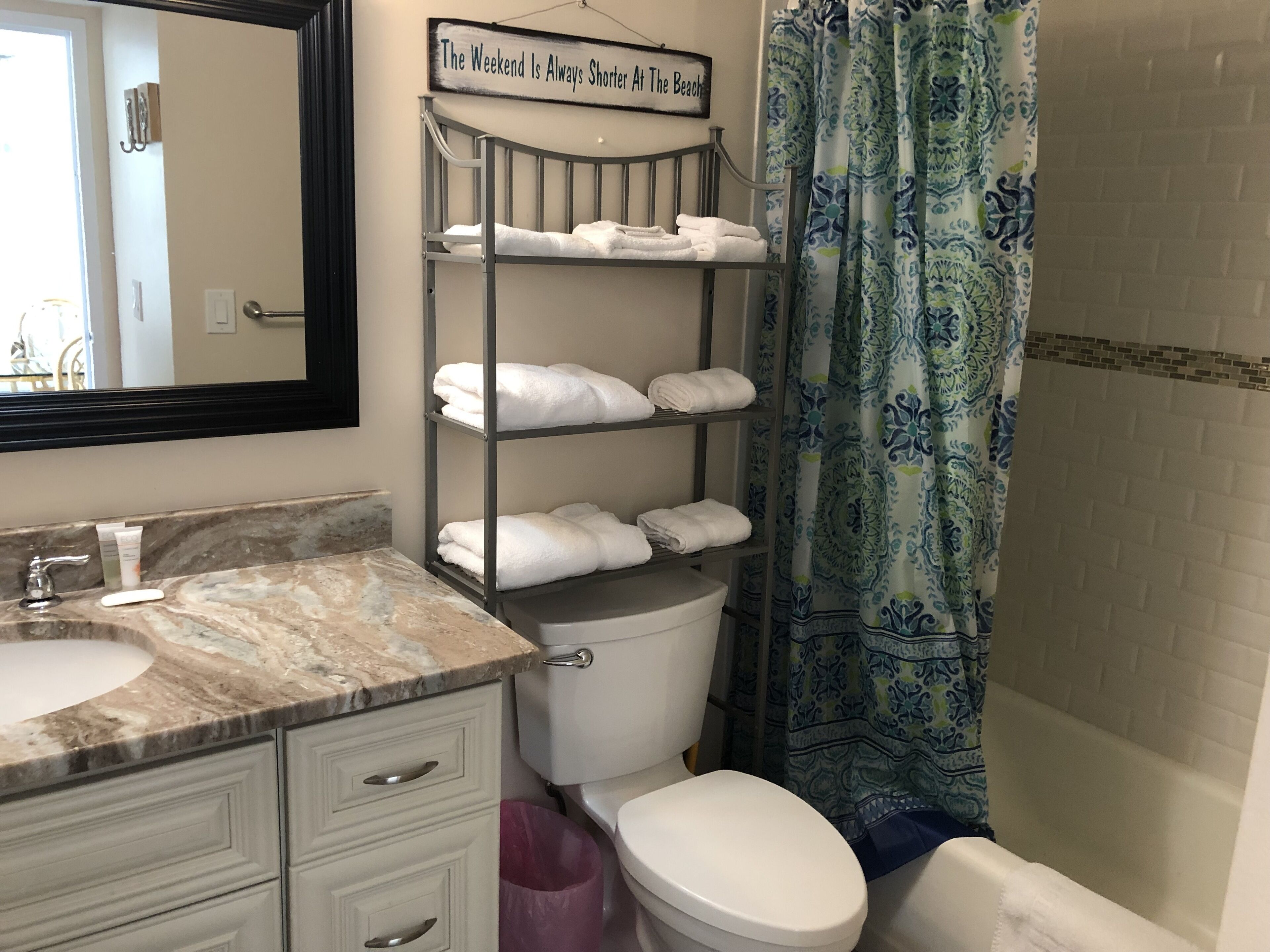 A bathroom with a marble sink, a toilet, a shelf with folded towels, and a shower curtain with a pattern.