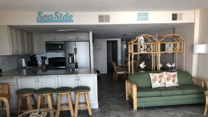 A modern kitchen with white cabinets, a stainless steel refrigerator, and a bar area with stools. - Direct Oceanfront Condo remodeled with Breathtaking Views from two private decks (Ocean City)