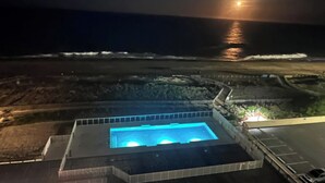 A pool with a blue-lit interior, surrounded by a landscaped area with a view of the ocean. - Direct Oceanfront Condo remodeled with Breathtaking Views from two private decks (Ocean City)