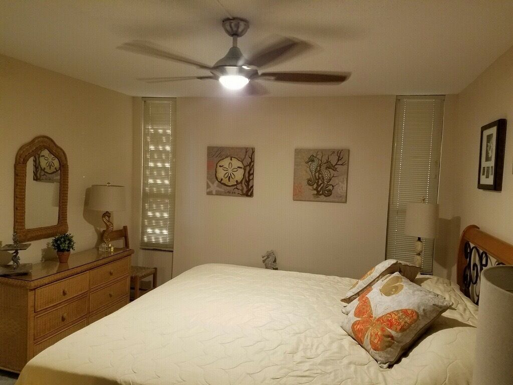 Un dormitorio con cama, cómoda, ventilador de techo y obras de arte en las paredes.