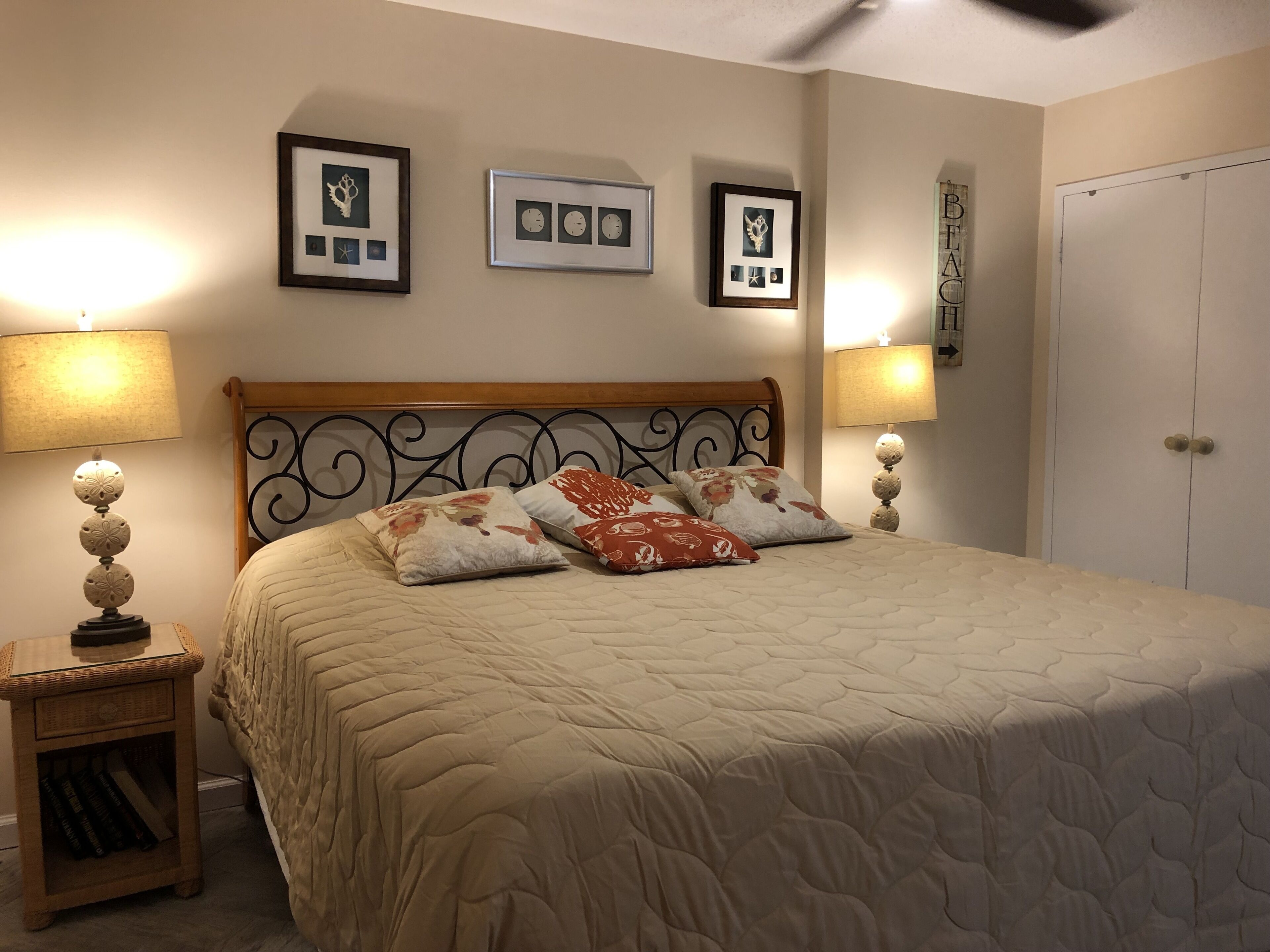 A neatly made bed with a quilted cover, two bedside lamps, a small bedside table with a lamp, and three framed pictures on the wall.