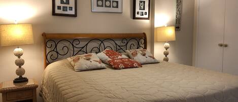 A neatly made bed with a quilted cover, two bedside lamps, a small bedside table with a lamp, and three framed pictures on the wall.