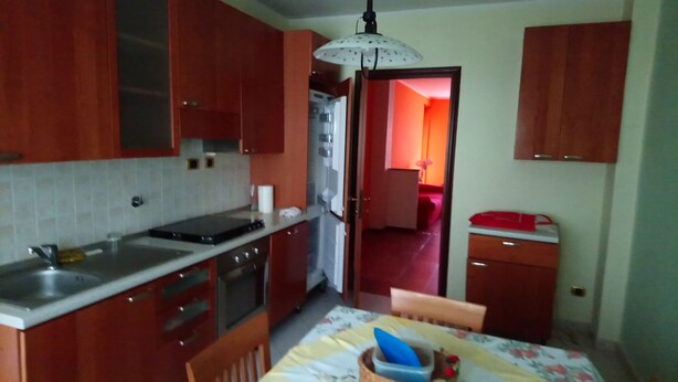 A compact kitchen with wooden cabinets, a sink, and a stove. There is a dining table with a floral tablecloth and a chair. - inn Stellone of Marco Pastore (Villastellone)