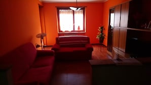 A living room with a red sofa, a standing fan, and a window with curtains. - inn Stellone of Marco Pastore (Villastellone)