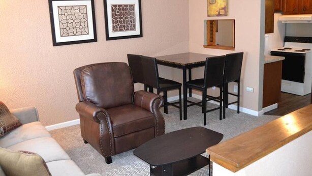 A living room with a brown leather armchair, a dining table with chairs, a kitchen area with a stove, and two framed wall art pieces. - Discover "a Perfect Place" in Grand Forks (Grand Forks)