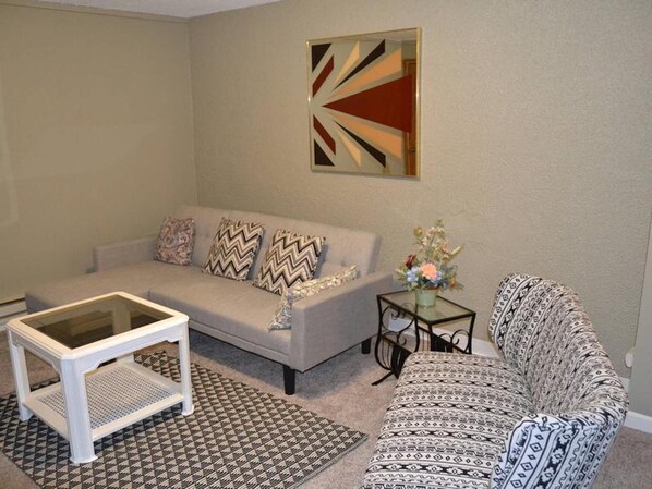 Un salon comprenant un canapé, une table basse, un tapis à motifs et un élément décoratif mural.