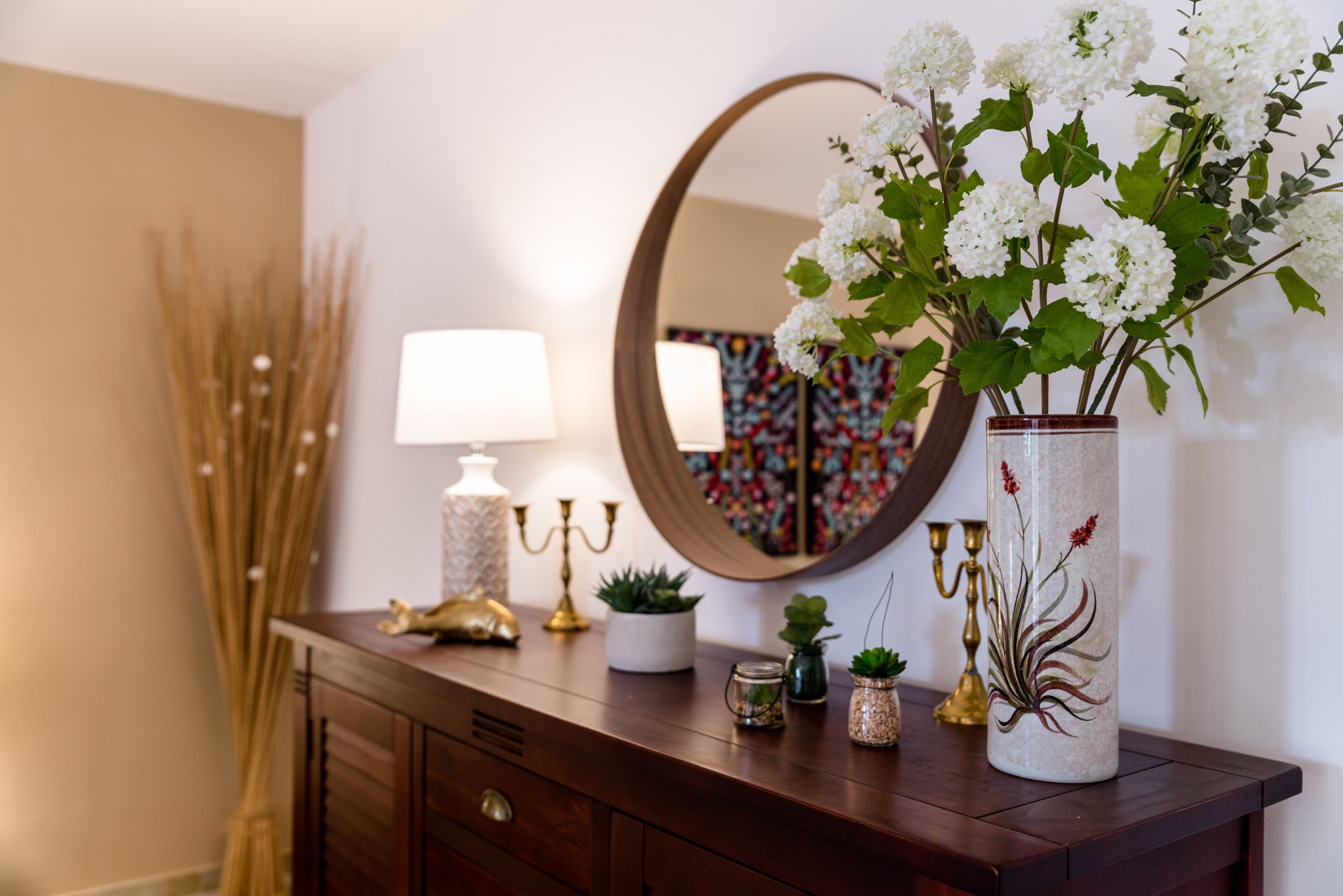 A wooden dresser with a mirror, a vase with white flowers, and various decorative items.
