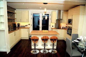 Una cocina moderna con una isla central, taburetes de bar y un comedor con mesa de vidrio y sillas.