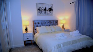 Ein Schlafzimmer mit einem großen Bett, zwei Nachttischen, einem Kopfteil und einem Gemälde an der Wand.