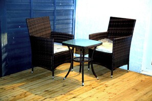 Un juego de silla y mesa de mimbre sobre un piso de madera, con una pared azul al fondo.