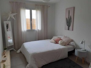 Relax in this serene bedroom with a large bed, a window with sheer curtains, and a cactus artwork above.