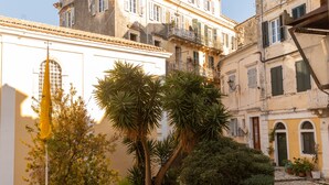 A courtyard with a flagpole, potted plants, and a building with balconies. - San Nicolo dei Vecchi Casa  by CorfuEscapes (Corfu)