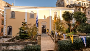 A building with a central entrance, a flag, and a flagpole. - San Nicolo dei Vecchi Casa  by CorfuEscapes (Corfu)