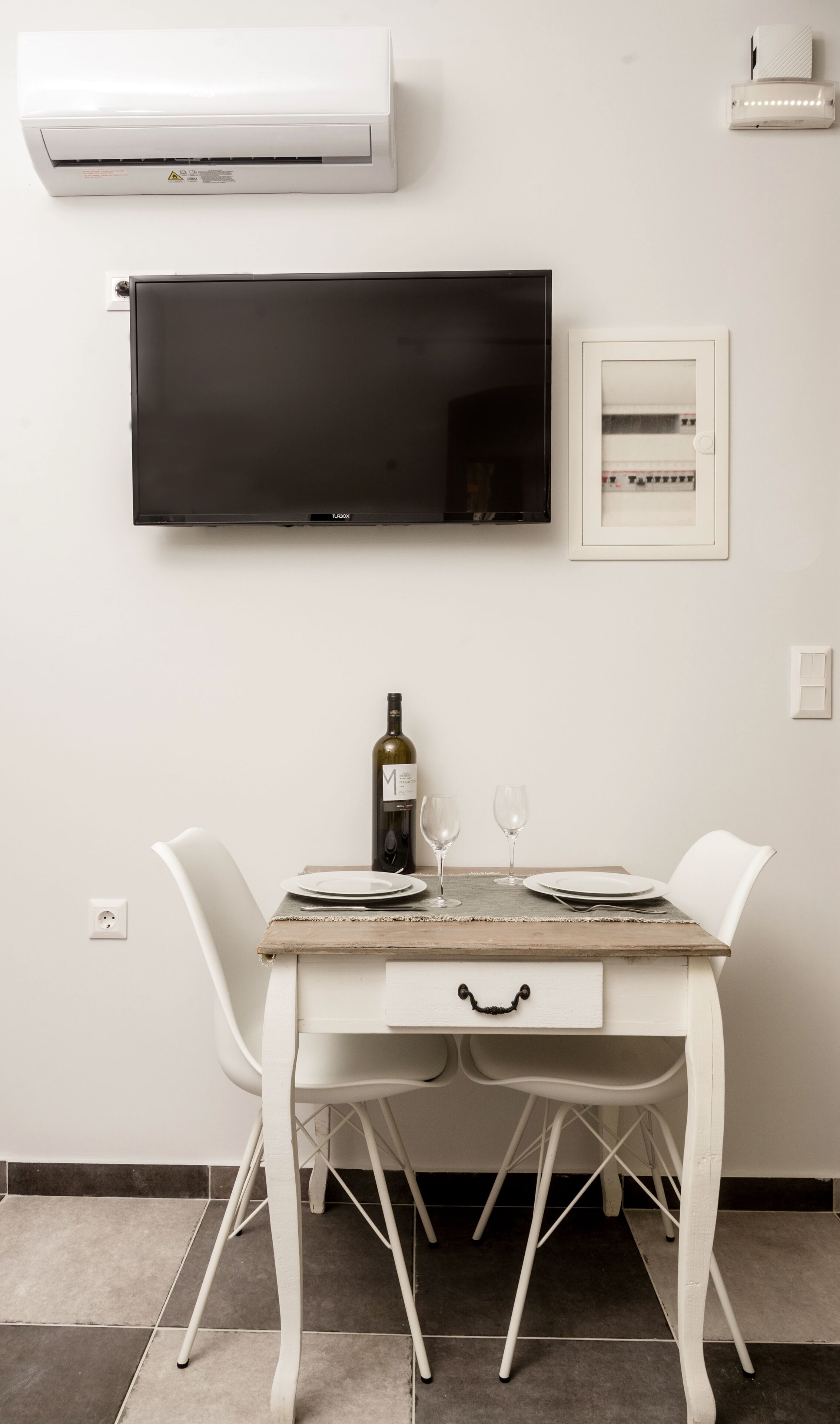 Un coin repas avec une table blanche, deux chaises, une bouteille de vin et deux verres à vin.