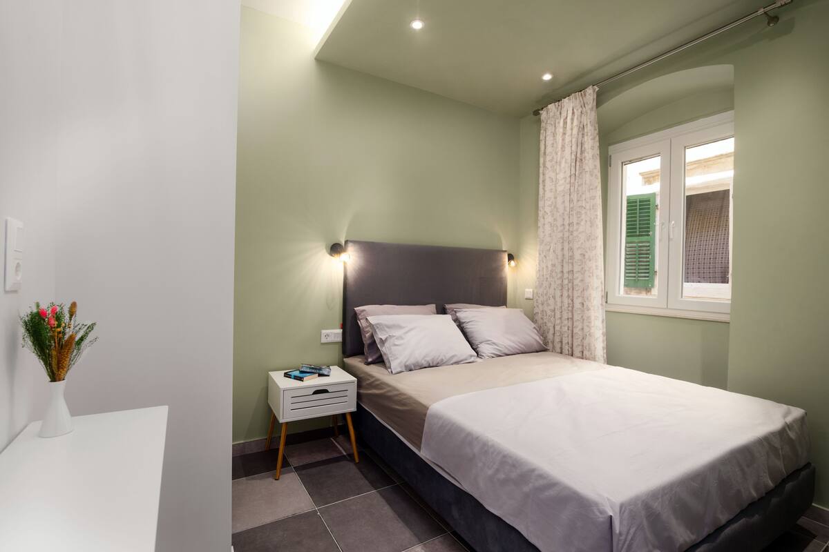 A bedroom with a bed, bedside table, and a window with curtains.