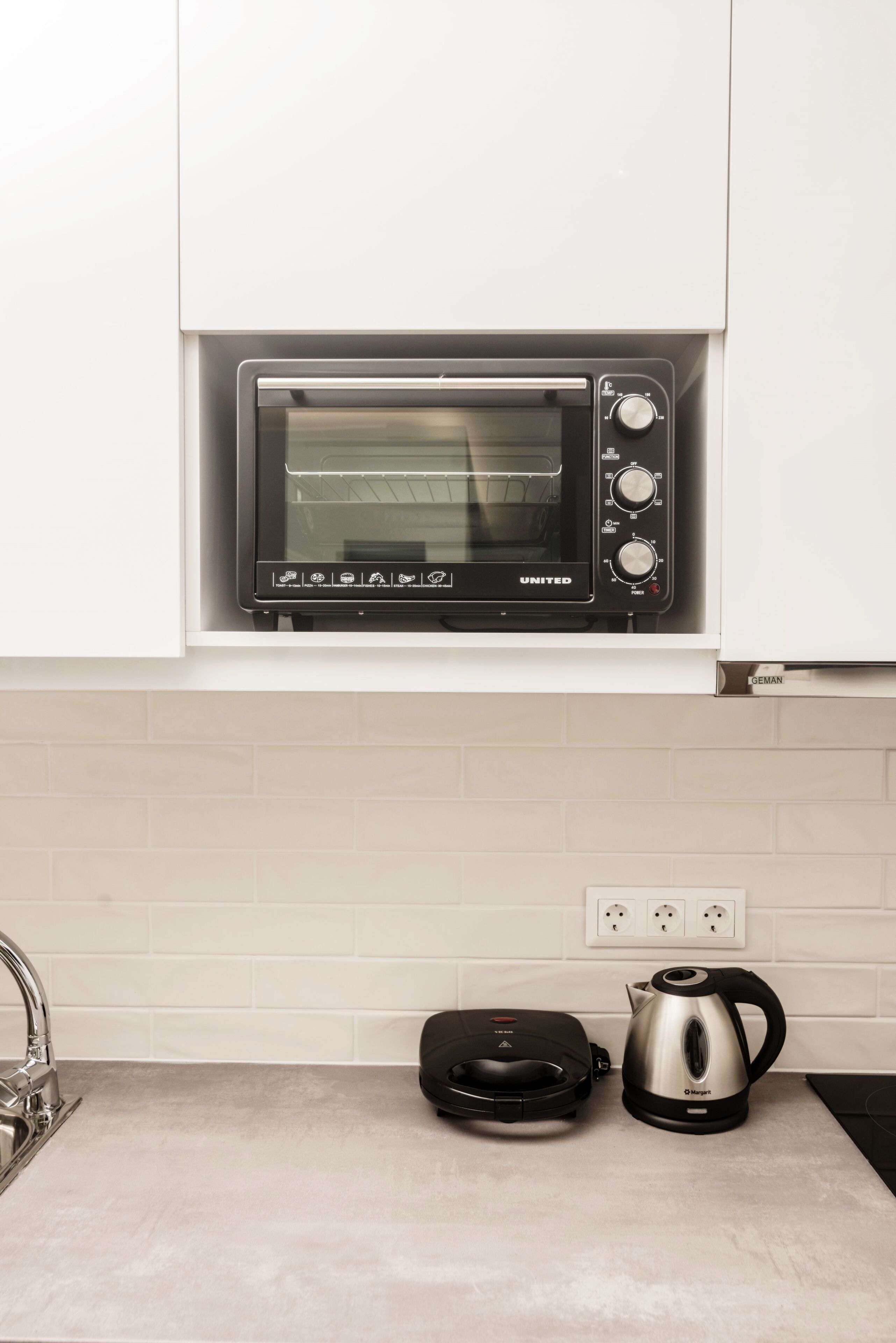 A kitchen with a built-in oven, a kettle, and a toaster.
