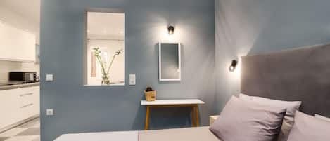 A bedroom with a bed, bedside table, and a small desk with a lamp.