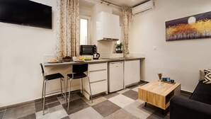 A compact kitchen with a dining area, a flat-screen TV mounted on the wall, and a painting above the sofa. - Eden Apartments  by CorfuEscapes (Corfu)