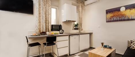 Una cocina compacta con zona de comedor, un televisor de pantalla plana montado en la pared y un cuadro sobre el sofá.