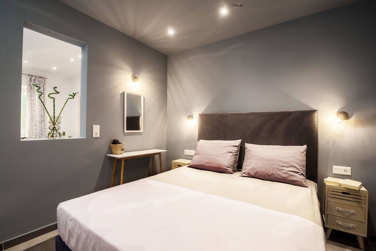 A modern bedroom with a large bed, bedside tables, a mirror, and a window with a plant.