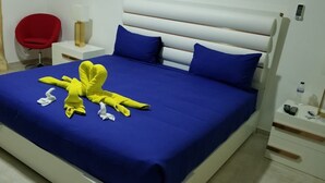 A neatly made bed with blue bedding, a red chair, a bedside table with a lamp, and a bottle of water.