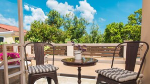 Un balcon avec deux chaises et une table, entouré d’une clôture en bois et de verdure.