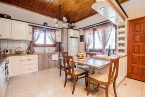 A kitchen with wooden cabinets, a central island with chairs, a refrigerator, and a dining table.