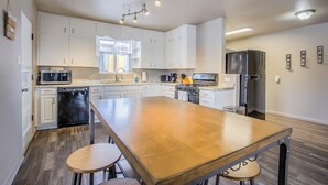 A modern kitchen with white cabinets, a wooden island, stainless steel appliances, and a large window.