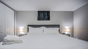 A neatly made bed with white linens, two bedside lamps, and a small stack of folded towels on the left side.