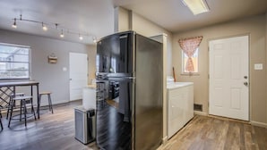 A modern kitchen with a stainless steel refrigerator, a dining area with stools, and a window with curtains.
