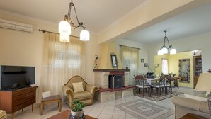 A spacious living room with a fireplace, a dining area, and a television. - Villa Southern Comfort by CorfuEscapes (Corfu)