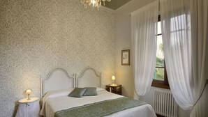 A bedroom with a bed, two bedside tables, a radiator, and a window with curtains.